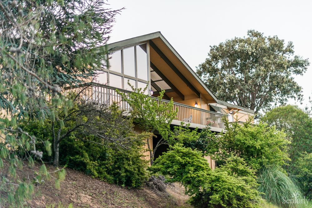 A house with a wooden balcony surrounded by lush greenery.