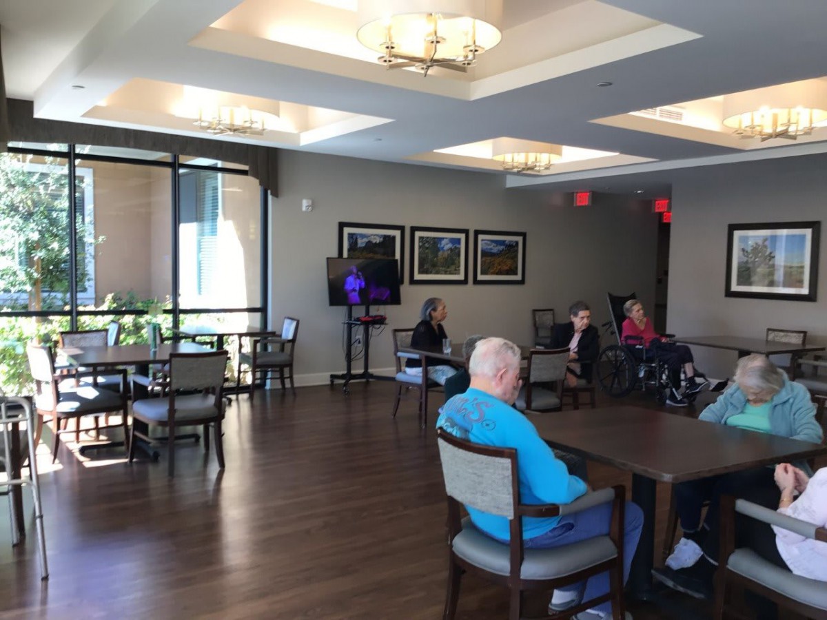 A group of seniors gather in a community center room with tables and chairs.