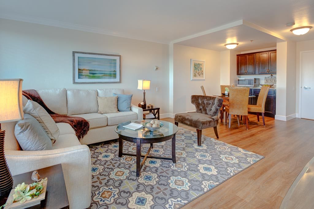 A cozy living room with a comfortable sofa, glass coffee table, and patterned rug, opening to a dining area.