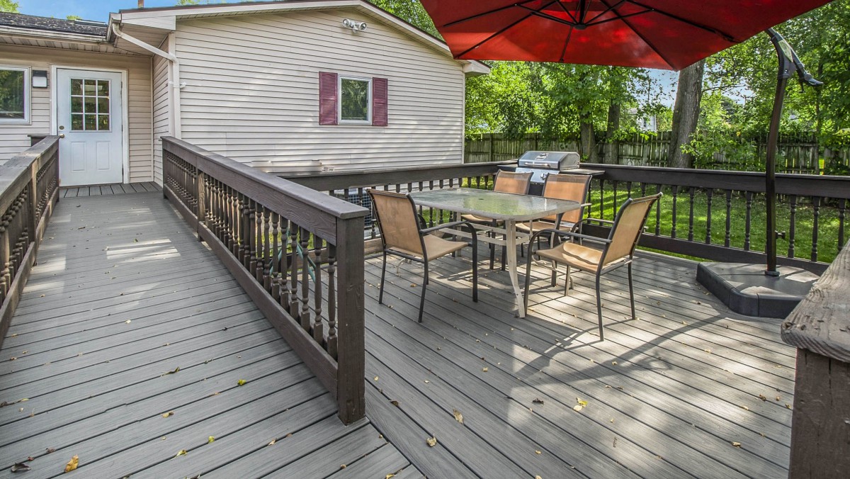 An outdoor deck with a table and chairs, shaded by a large umbrella.