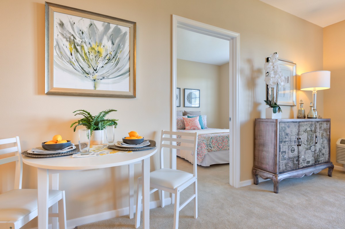 A cozy dining area with a white table and chairs, set for two, adjacent to a bedroom featuring inviting decor.