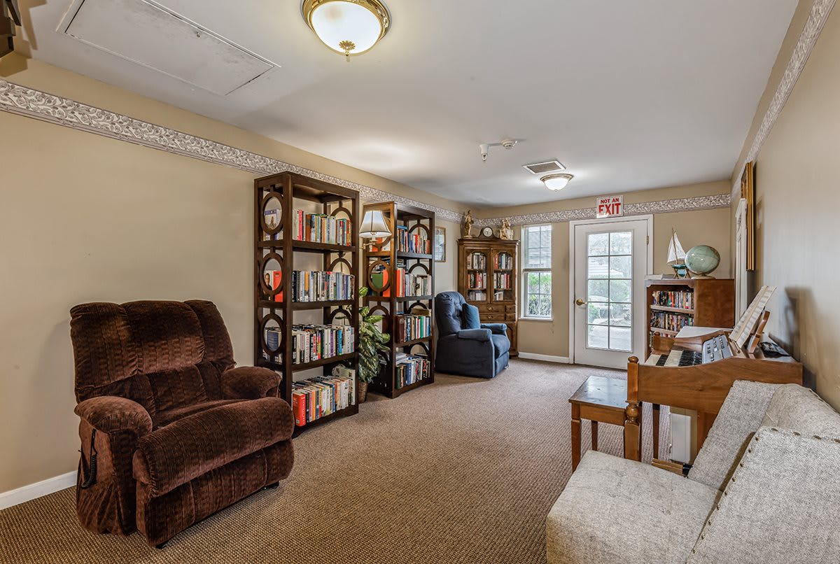 A cozy living room with bookshelves, an armchair, and a piano, creating a warm library-like atmosphere.
