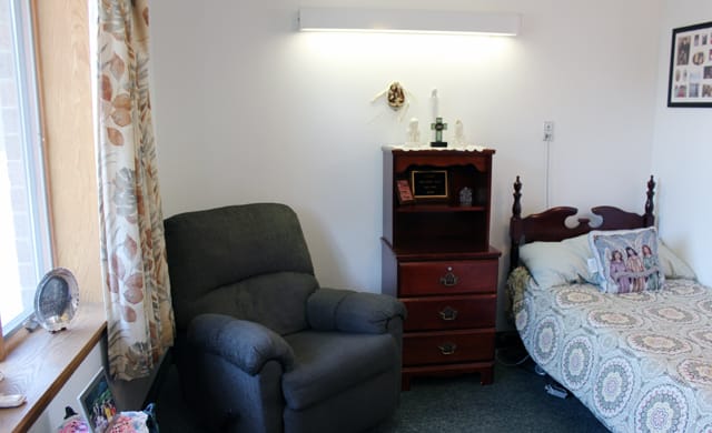 A cozy bedroom setup with an armchair and a wooden chest of drawers next to a bed.