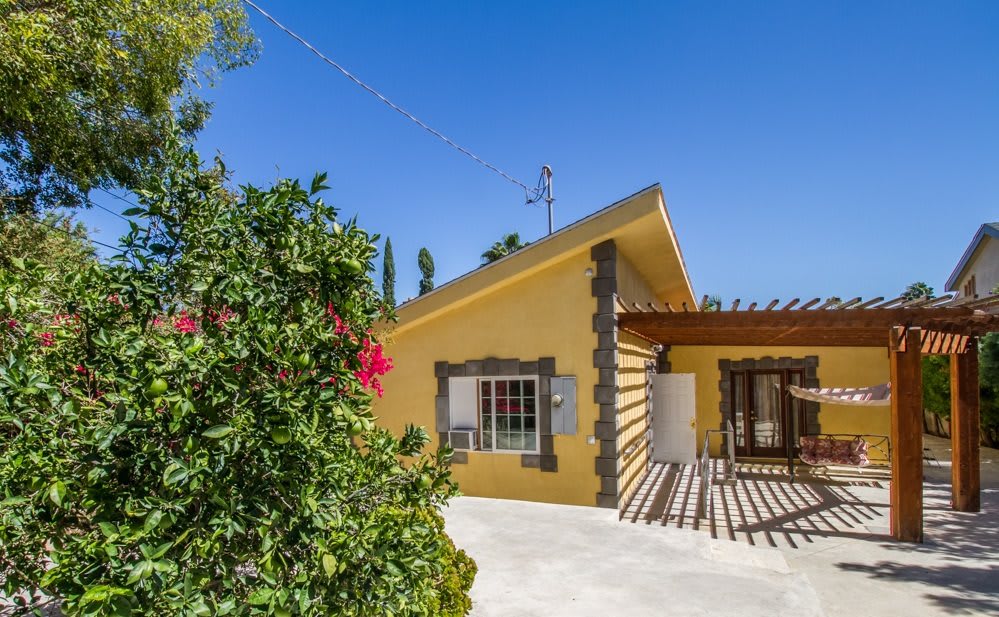 A charming yellow house with a garden under a clear blue sky.