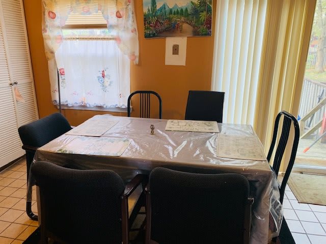 A dining room with a table covered in plastic, surrounded by chairs and adorned with a painting on the wall.