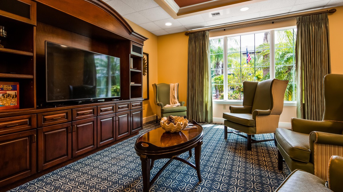 A cozy living room with a wooden entertainment center, two armchairs, and a coffee table in front of a large window with curtains.