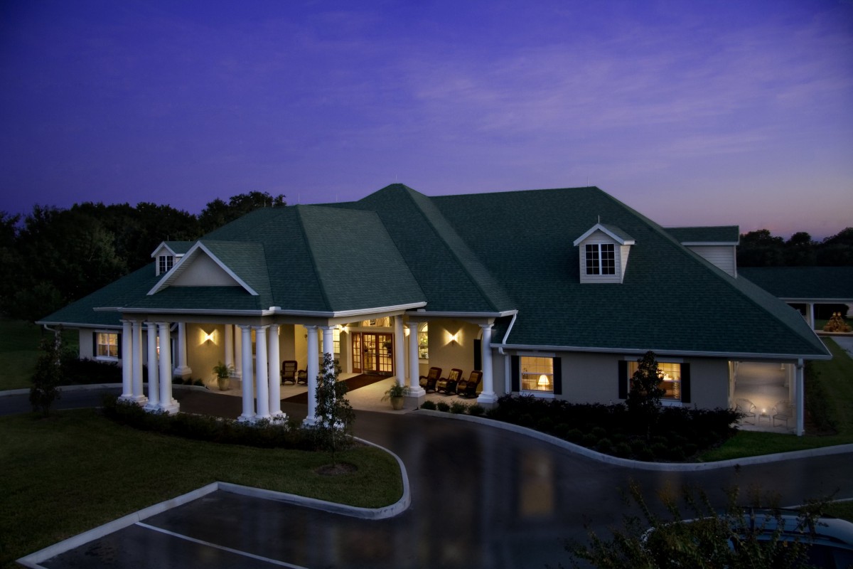 A well-lit house with a green roof and columns at dusk.