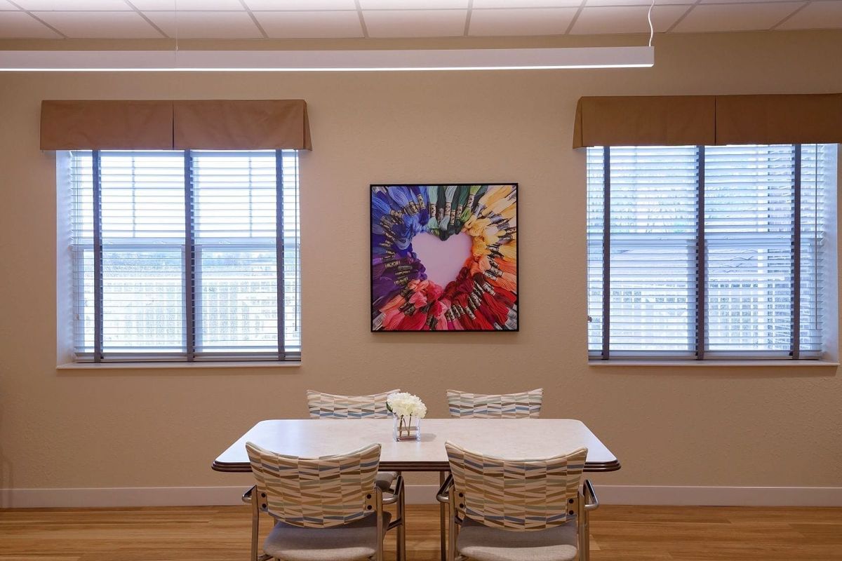 A cozy dining area with a table and chairs, adorned by a colorful painting on the wall.