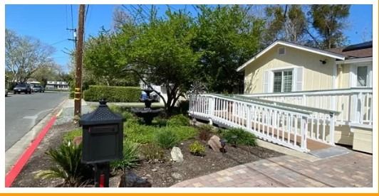 A house with a landscaped garden featuring a tree, ramp, and mailbox.