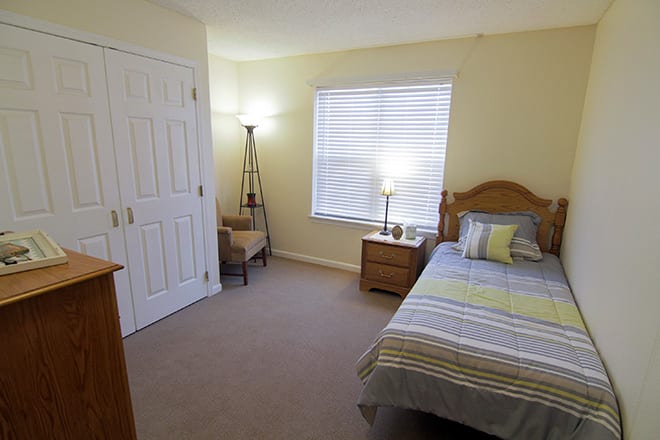 A cozy bedroom with a single bed, bedside table, and floor lamp.