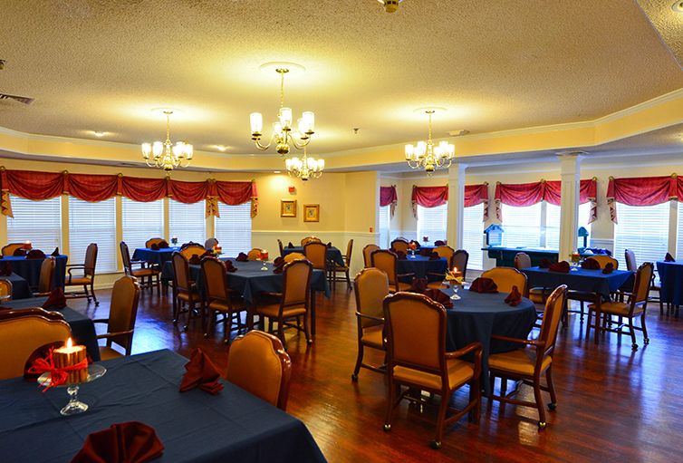 An elegant dining area with multiple tables and chairs, decorated with chandeliers and large windows.