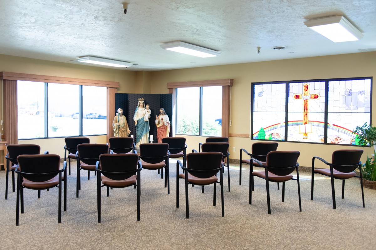 A small chapel with rows of chairs facing religious statues and windows.