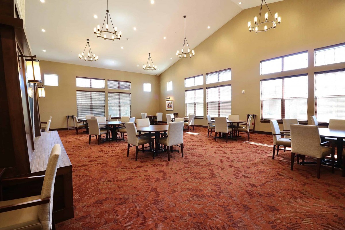A spacious dining area with chandeliers, tables, and chairs set on a carpeted floor.