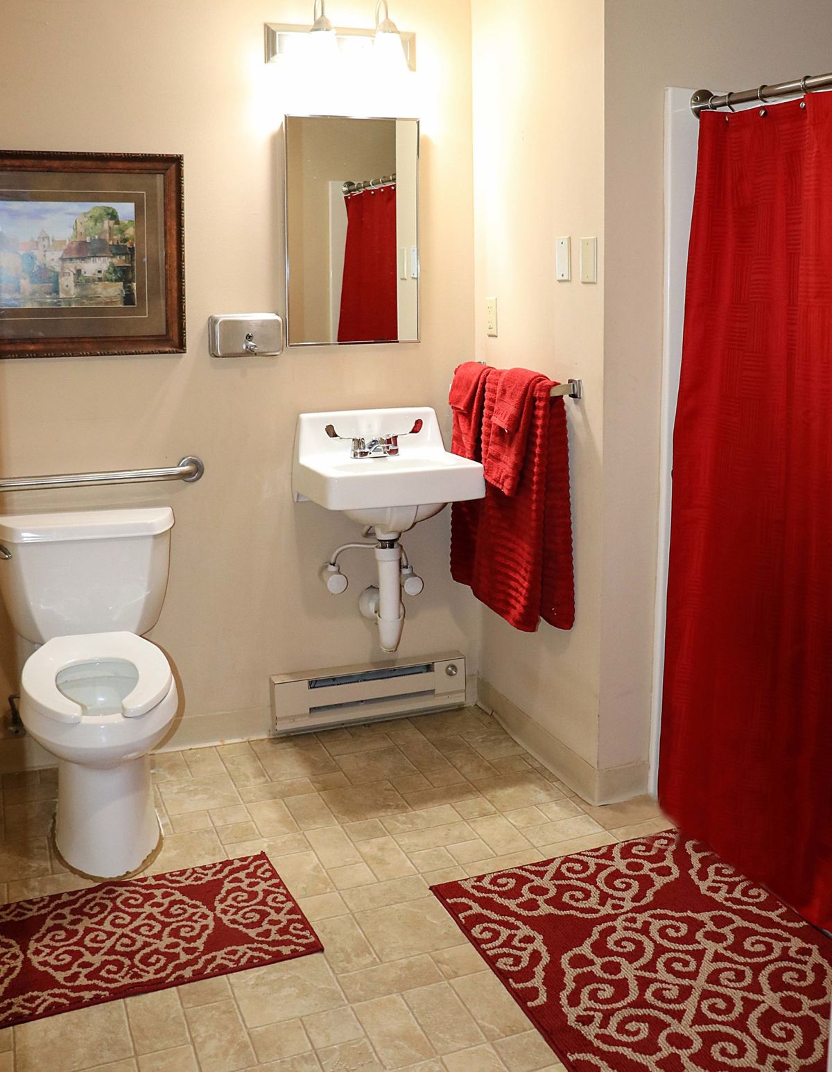 A bathroom with red accents, featuring a sink, toilet, and mirror.