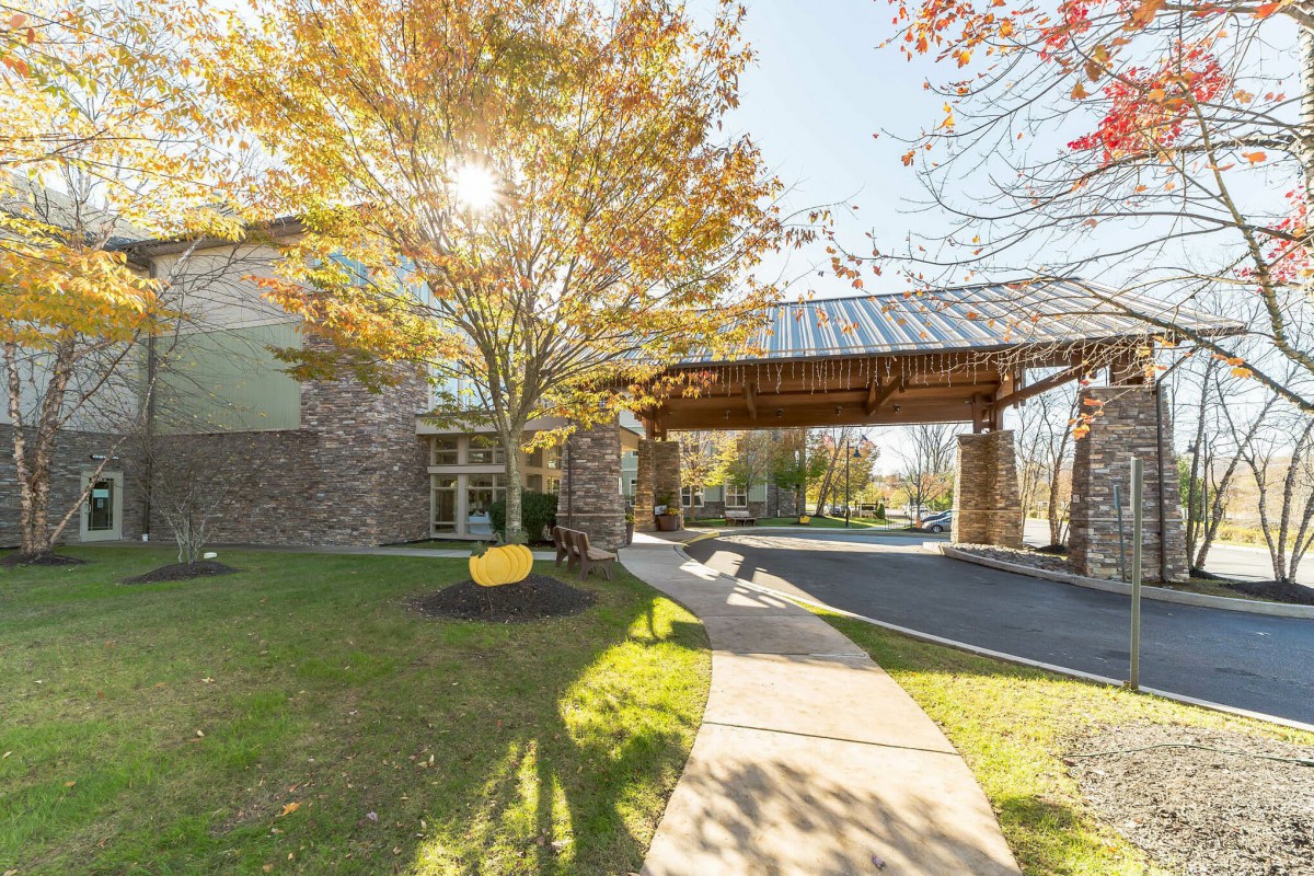 A building entrance with a covered walkway, surrounded by autumn trees and landscaping.
