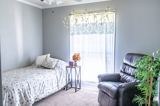 A serene and cozy bedroom featuring a bed, recliner, and soft natural light filtering through the curtains.