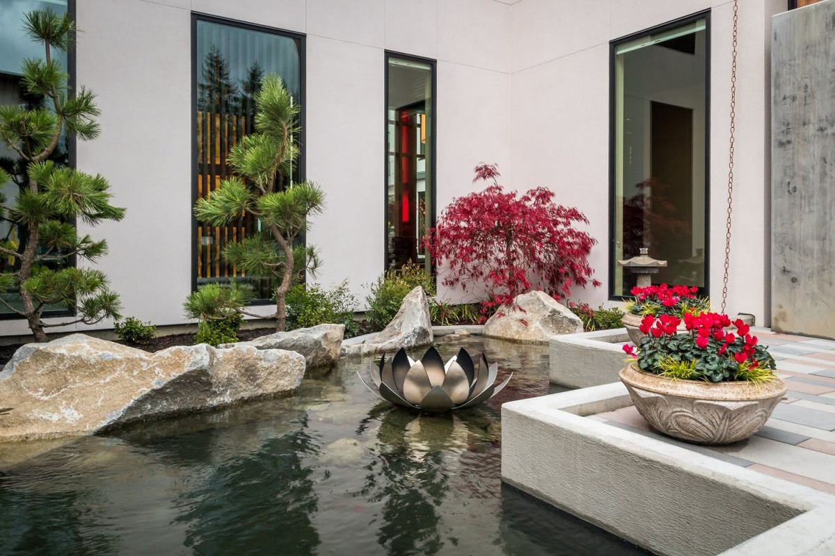 A tranquil courtyard featuring a pond with a water feature, surrounded by lush greenery and modern architecture.