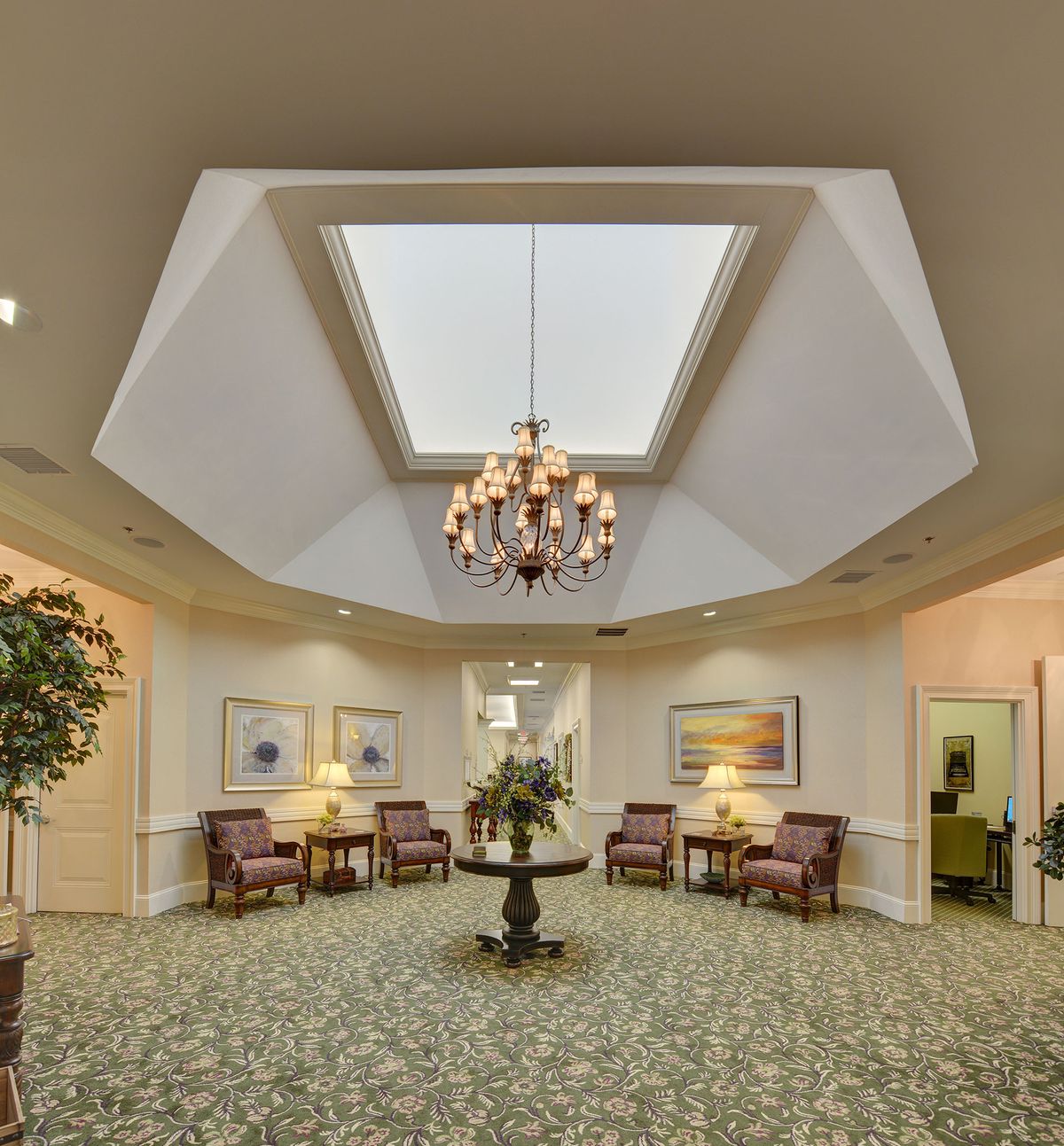 A well-lit lobby featuring a central chandelier, skylight, and comfortable seating arrangements.