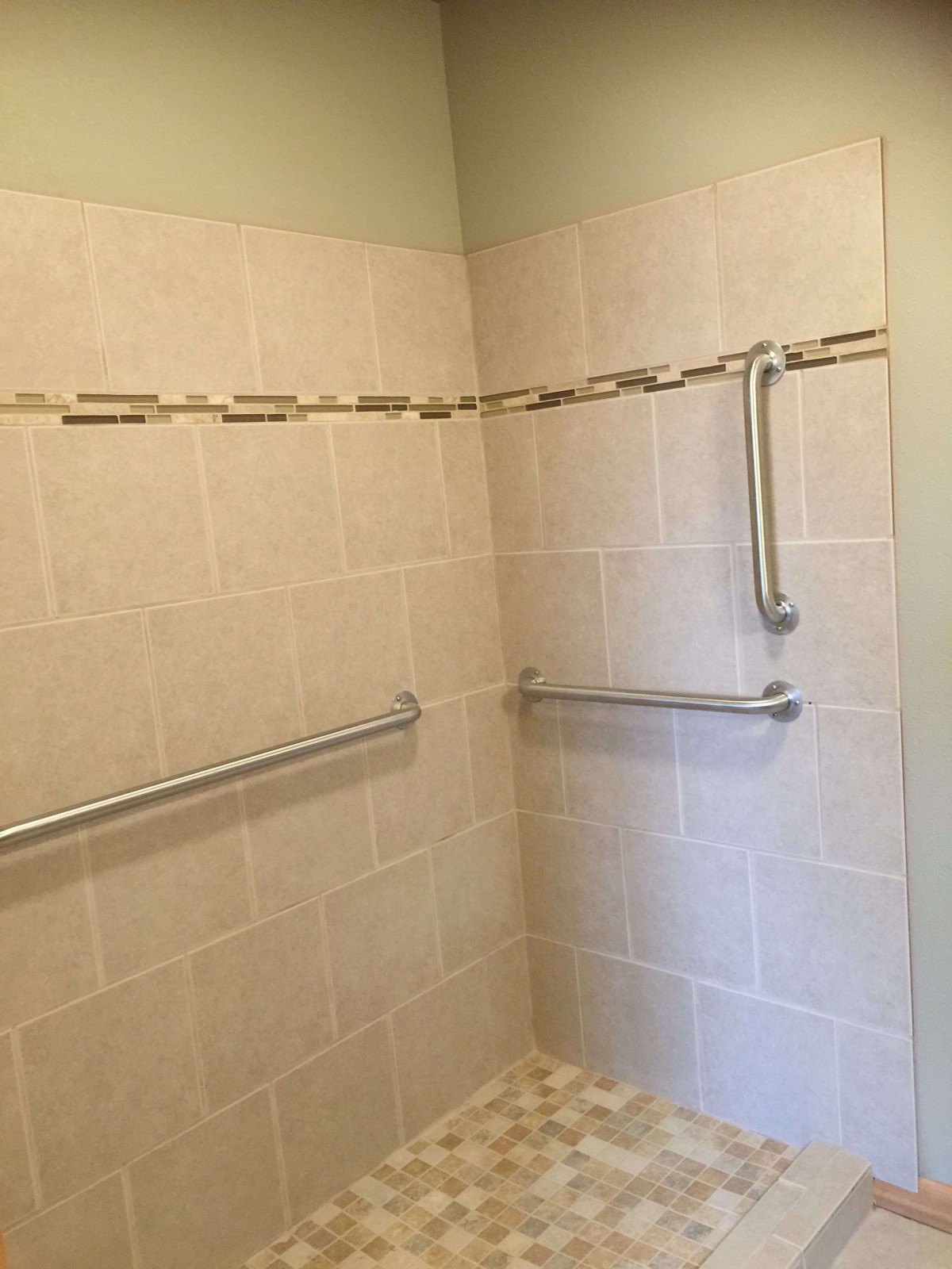 A bathroom shower with tiled walls and safety handrails.