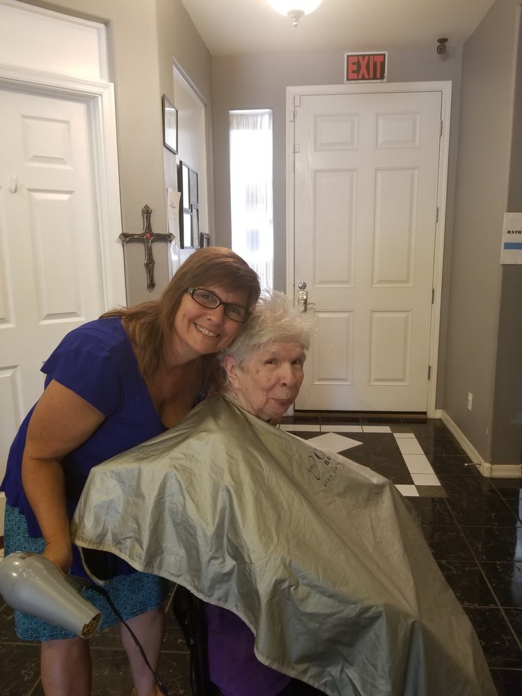 A woman smiles while giving an elderly person a haircut at home.