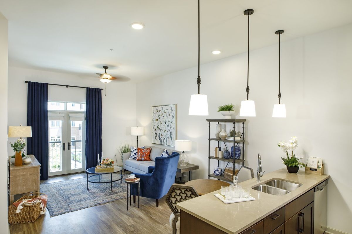 A modern open-plan living room and kitchen featuring a blue armchair, pendant lighting, and wood flooring.