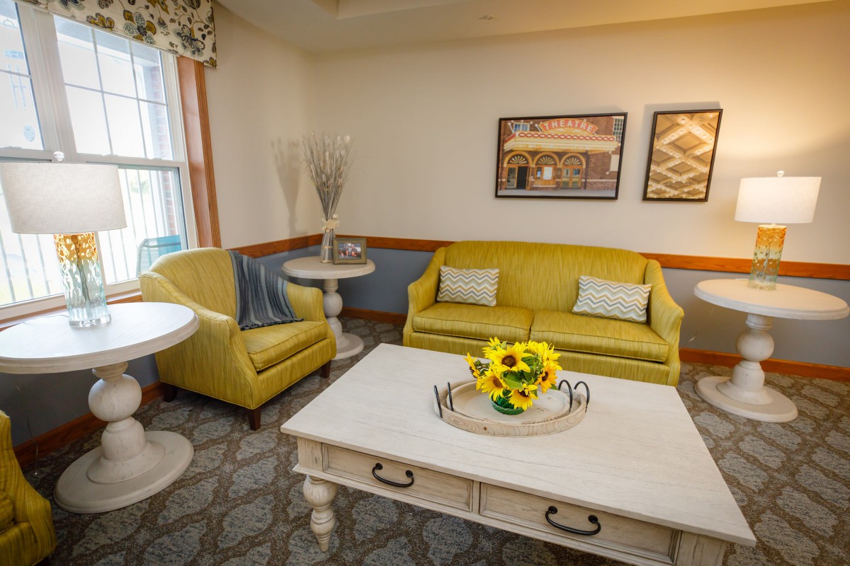 A cozy living room with yellow sofas, a white coffee table adorned with sunflowers, and tasteful wall art.