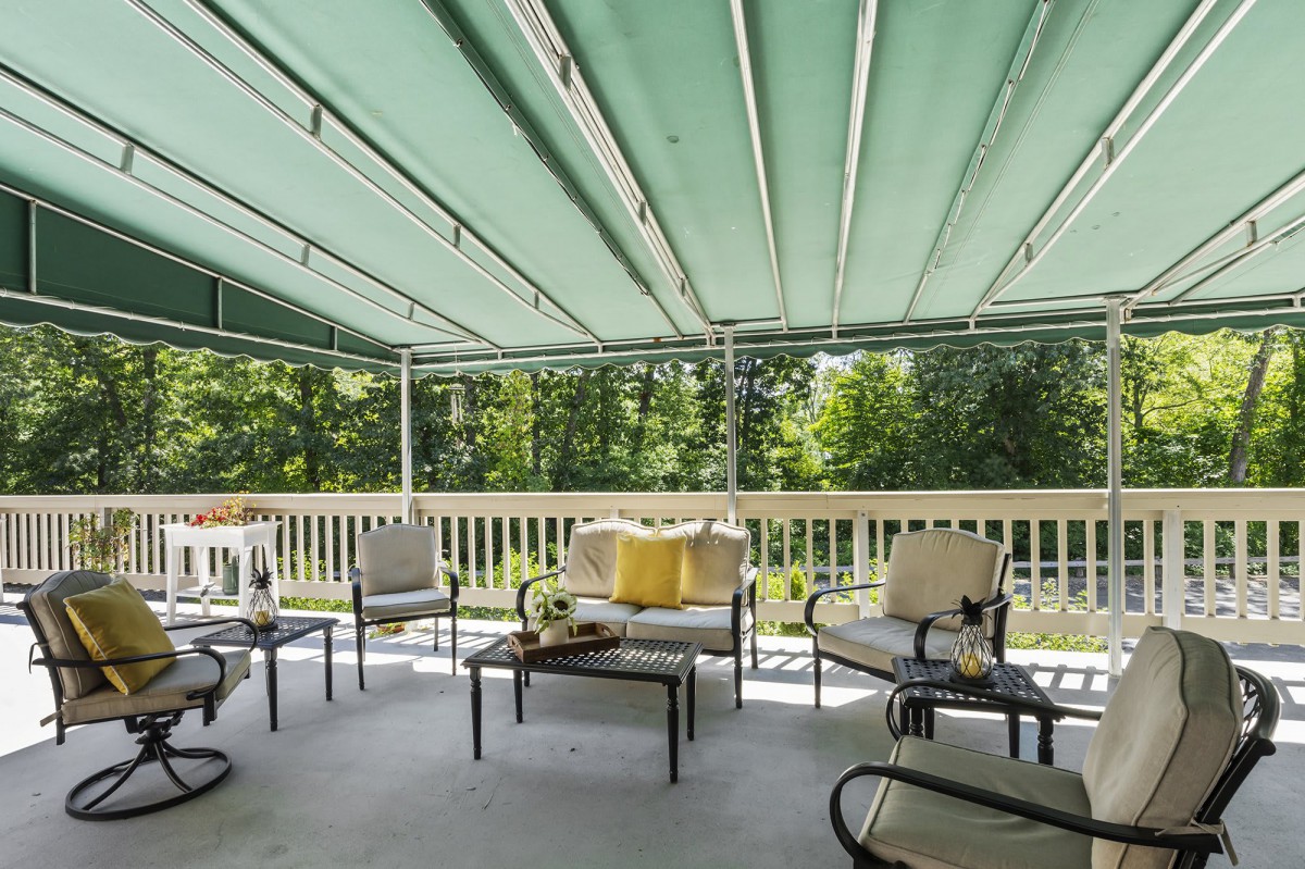 A cozy outdoor patio with comfortable seating under a green canopy, overlooking a lush garden.