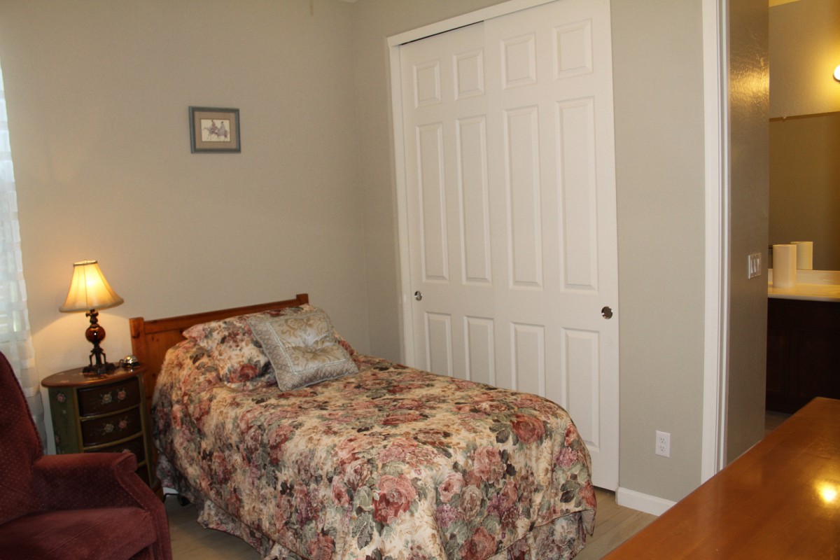 A cozy bedroom with a single bed featuring floral bedding and a closet with white doors.