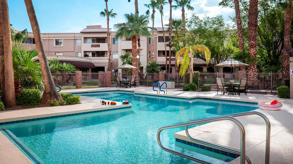 A luxurious swimming pool surrounded by palm trees and modern apartments, creating a perfect vacation atmosphere.
