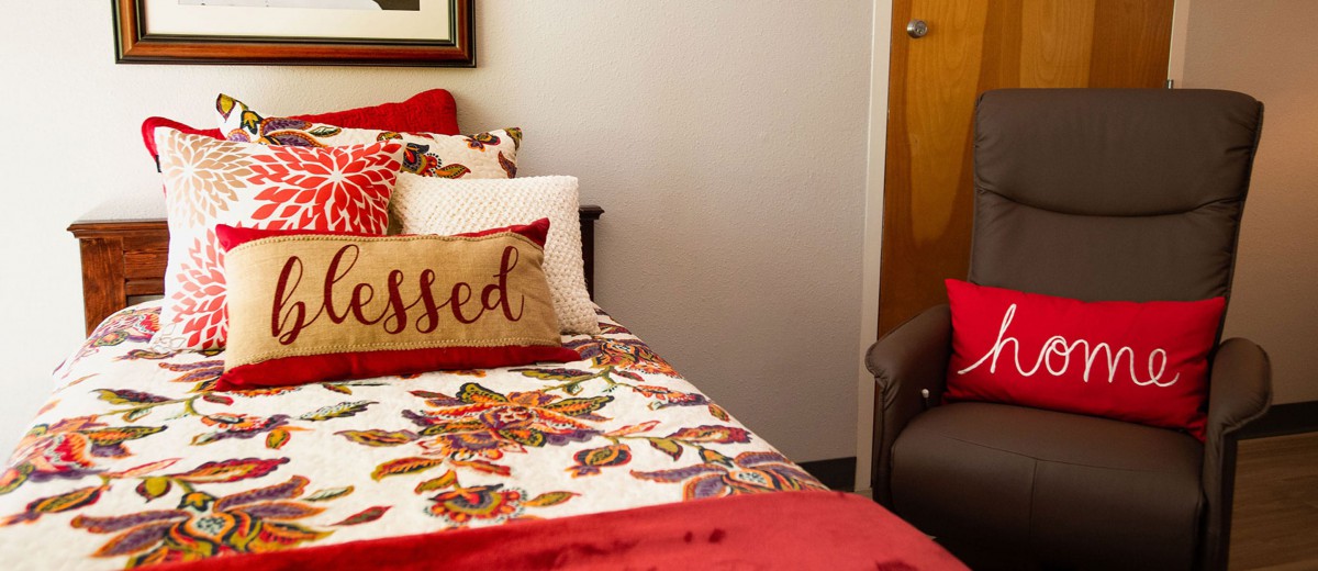 A cozy bedroom featuring a floral bedspread and decorative pillows, including one with the word 'blessed'.