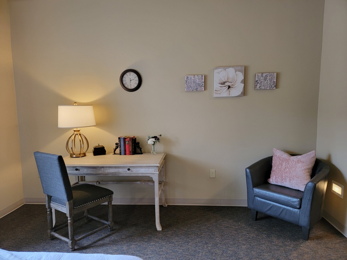 A cozy room with a desk and chair, adorned with wall art and a small sofa.