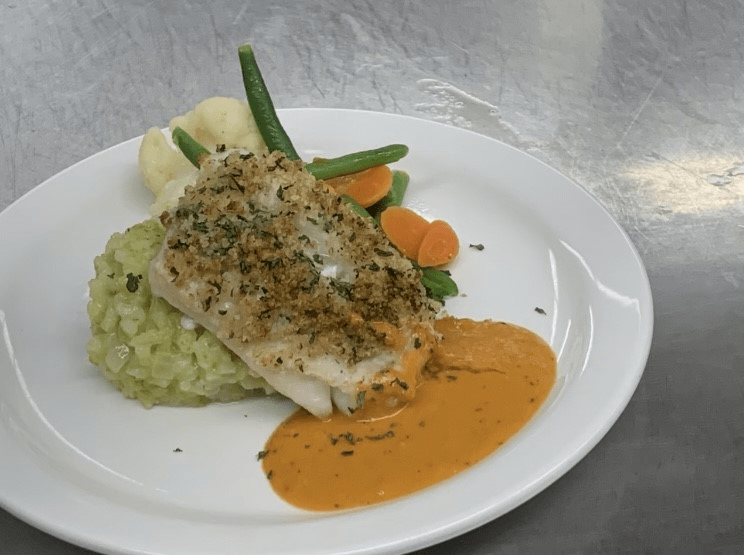 A gourmet fish dish served with mashed peas, vegetables, and a rich sauce.