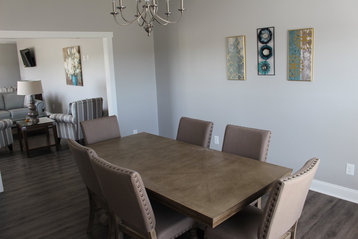 A modern dining room with a wooden table and upholstered chairs, decorated with wall art and a chandelier.