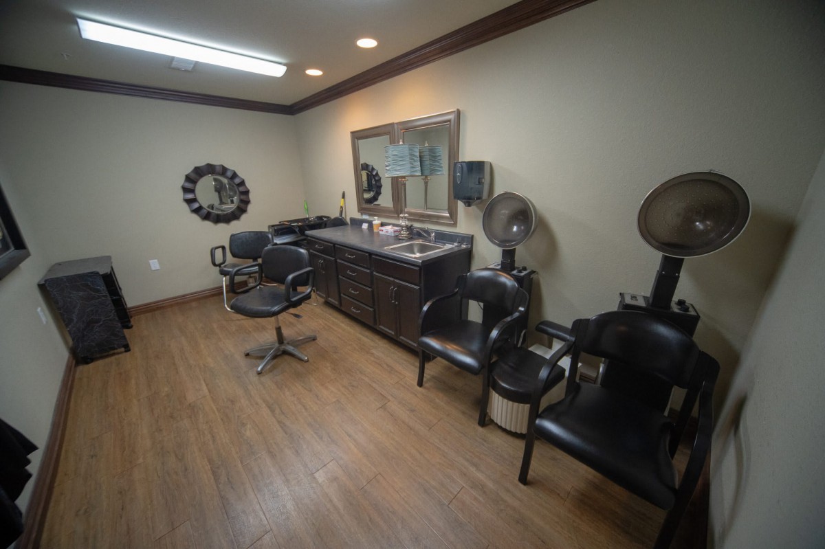 A neatly arranged hair salon with multiple chairs and hair dryers, featuring wooden flooring and a large mirror.