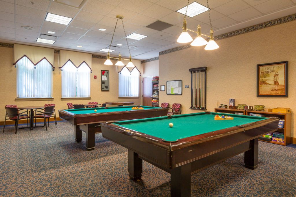A well-lit game room featuring multiple billiards tables and comfortable seating.