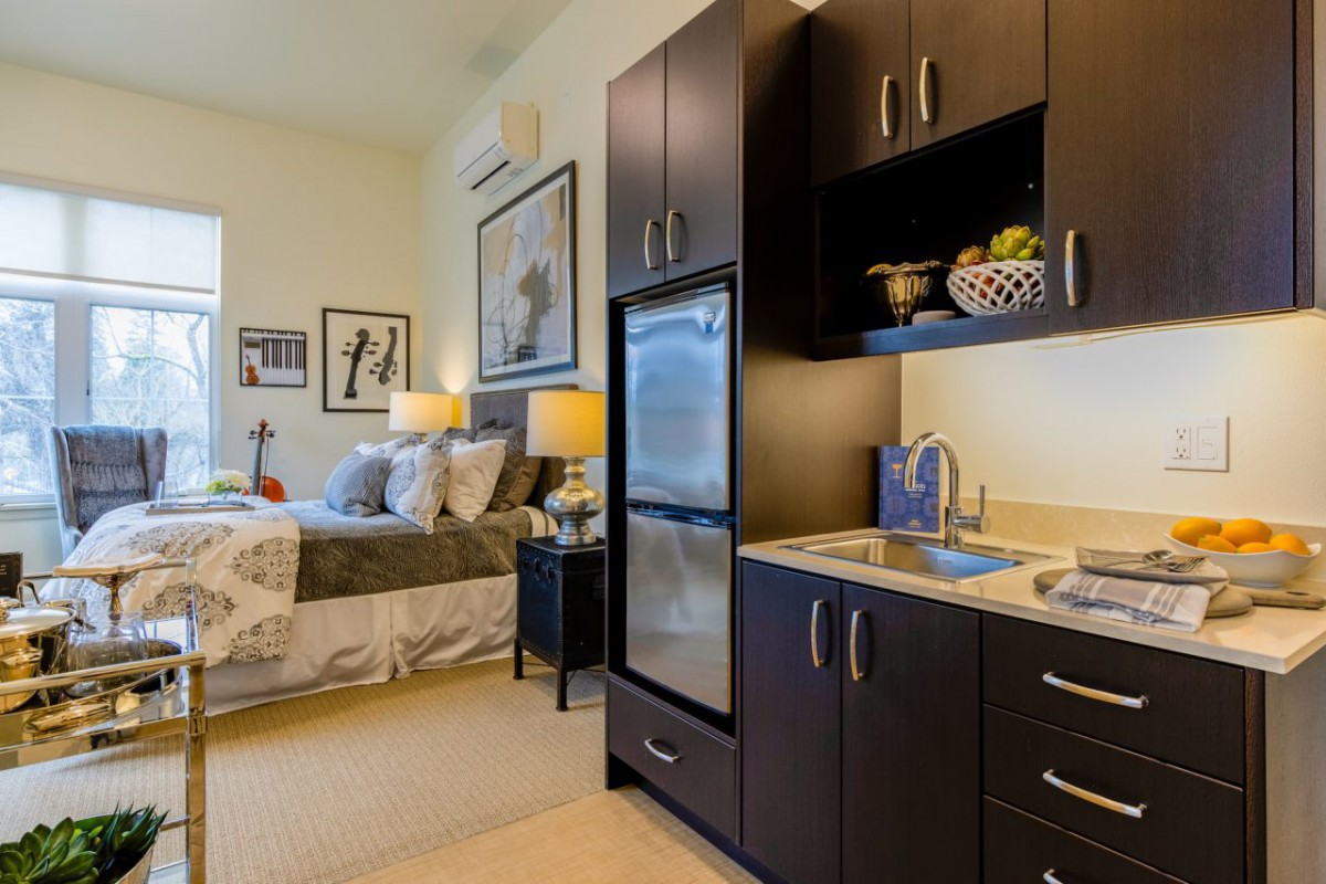 A cozy studio apartment featuring a compact kitchenette and a neatly arranged bedroom area.