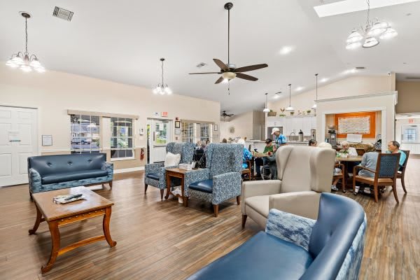 A spacious and modern living area featuring comfortable seating with blue and beige chairs, a wooden floor, and a ceiling fan for added comfort.