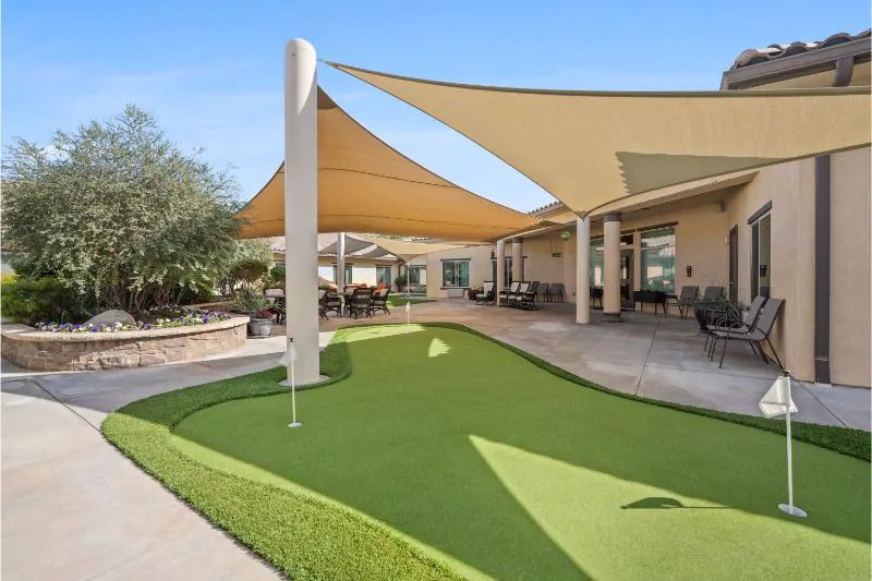 A sunny outdoor area featuring a putting green with shade sails and a patio.