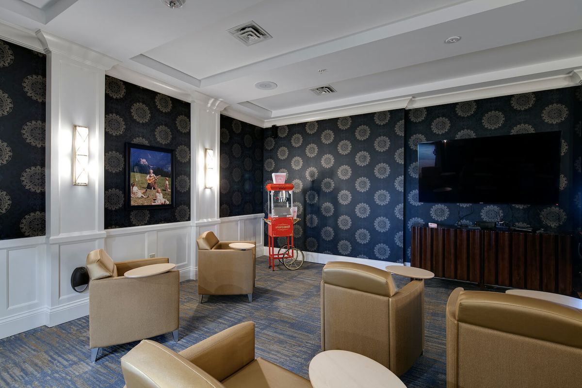 A modern lounge area featuring comfortable chairs, a television, and a popcorn machine against patterned wallpaper.