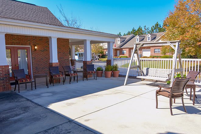 A sunny patio area with chairs and a swing, surrounded by suburban homes.