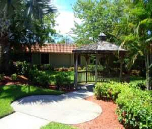 A serene garden with a gazebo surrounded by lush greenery and a paved pathway.
