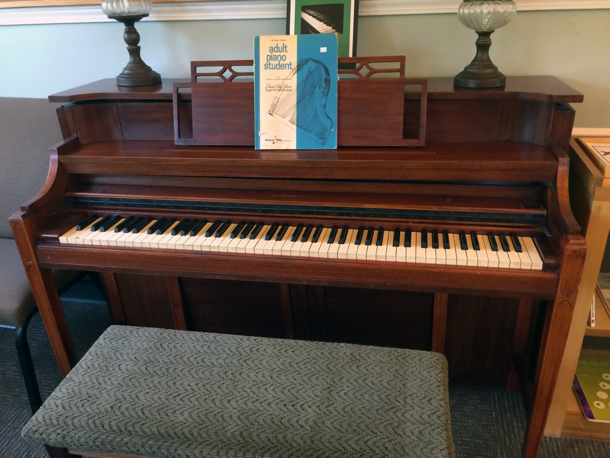 An upright piano with a music book placed on the stand, accompanied by a cushioned bench.