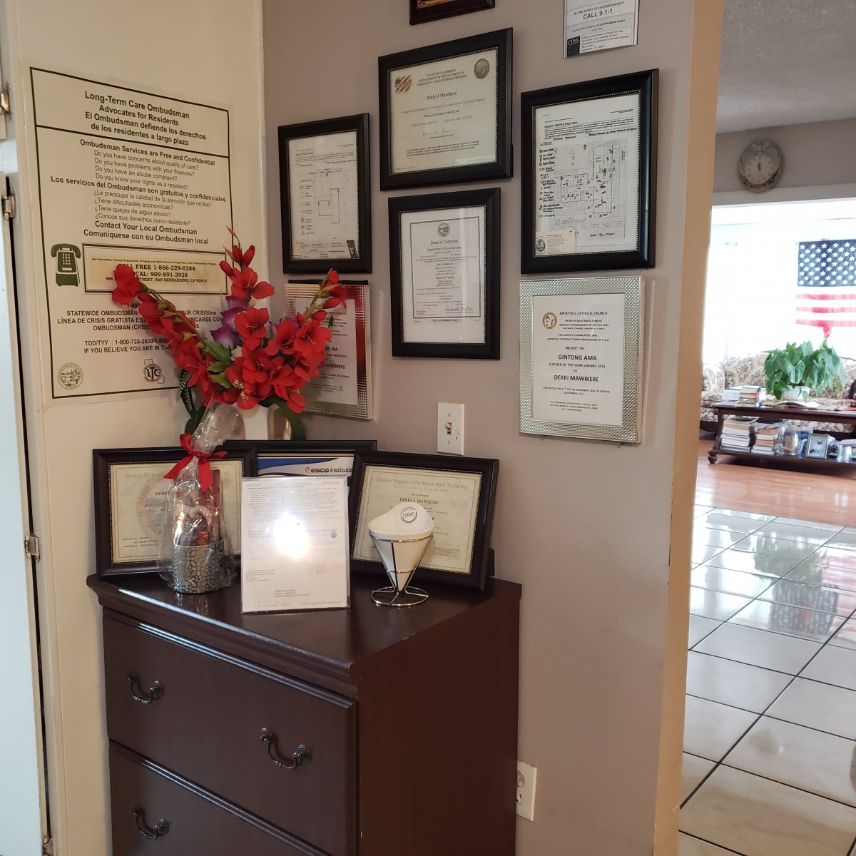 A cozy corner of a home showcasing framed certificates and awards on the wall above a dresser adorned with red flowers.
