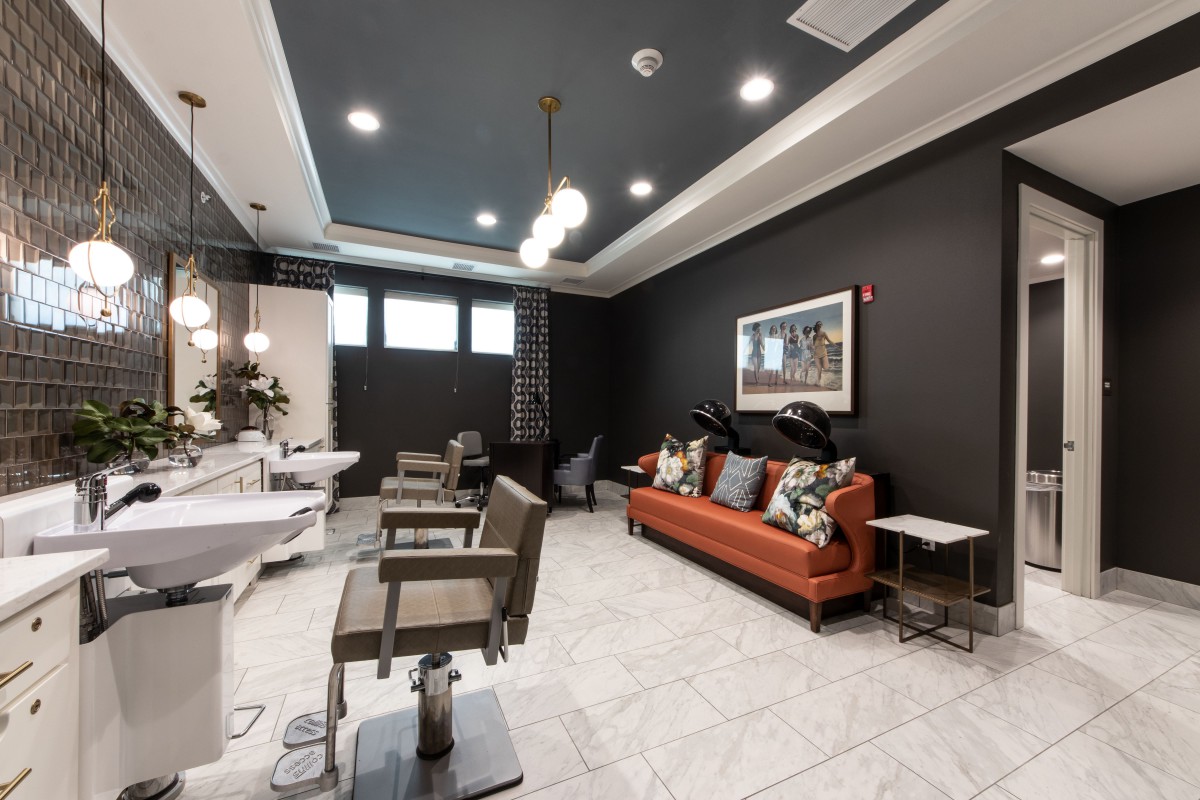 A modern hair salon interior featuring stylish chairs, a comfortable couch, and elegant lighting fixtures.