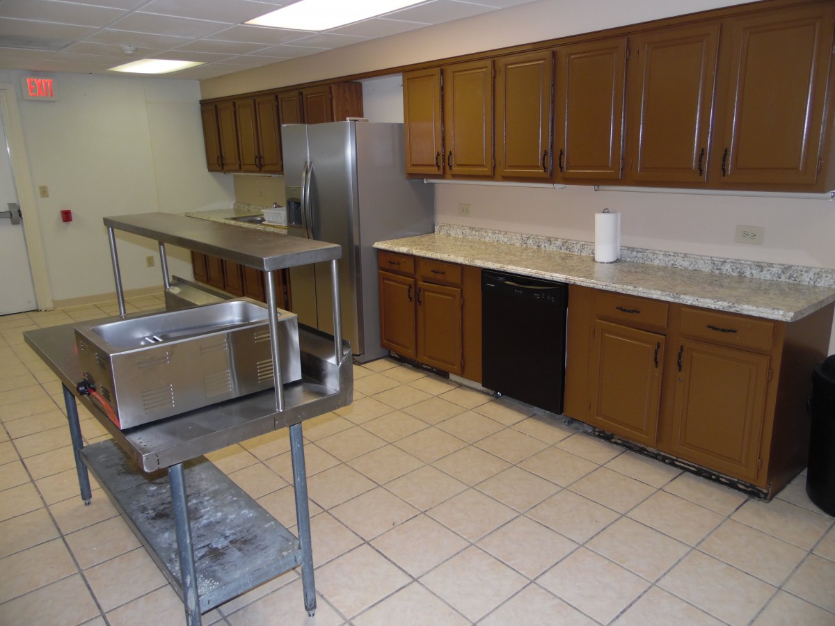 A commercial kitchen with wooden cabinets, stainless steel appliances, and a tiled floor.