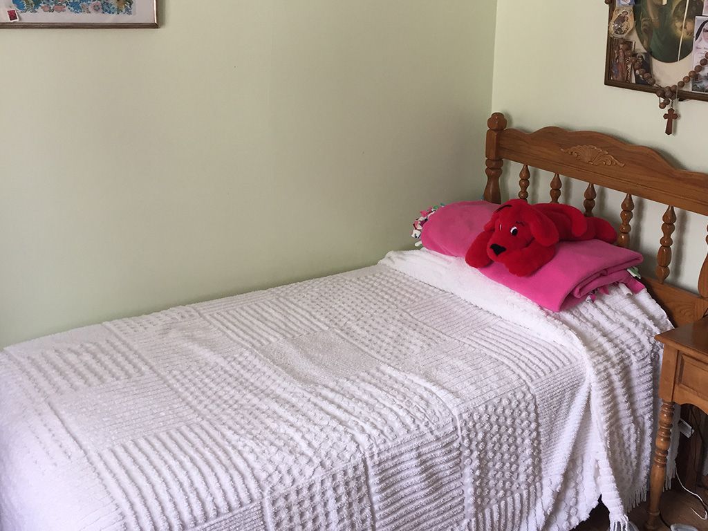 A cozy single bed with a striped bedspread and red teddy bear pillow in a softly lit bedroom.