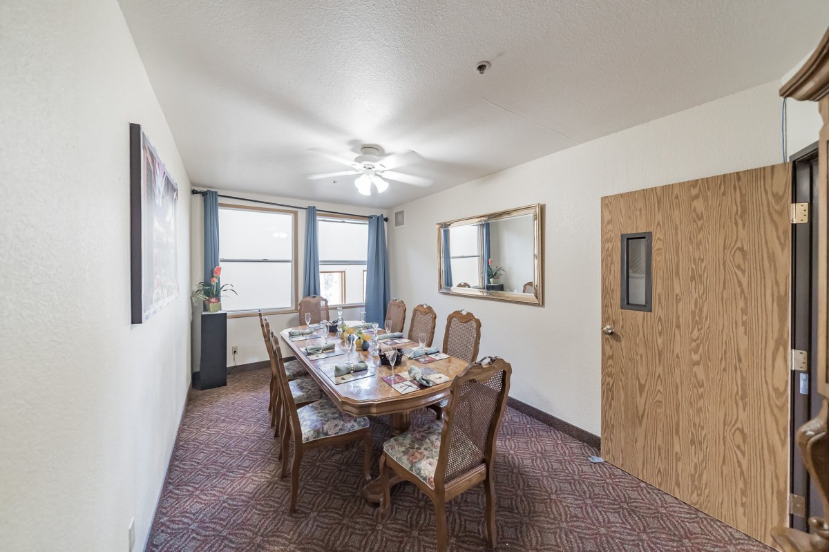 A well-lit dining room with a large table and six chairs, complete with a mirror on the wall and a ceiling fan overhead.