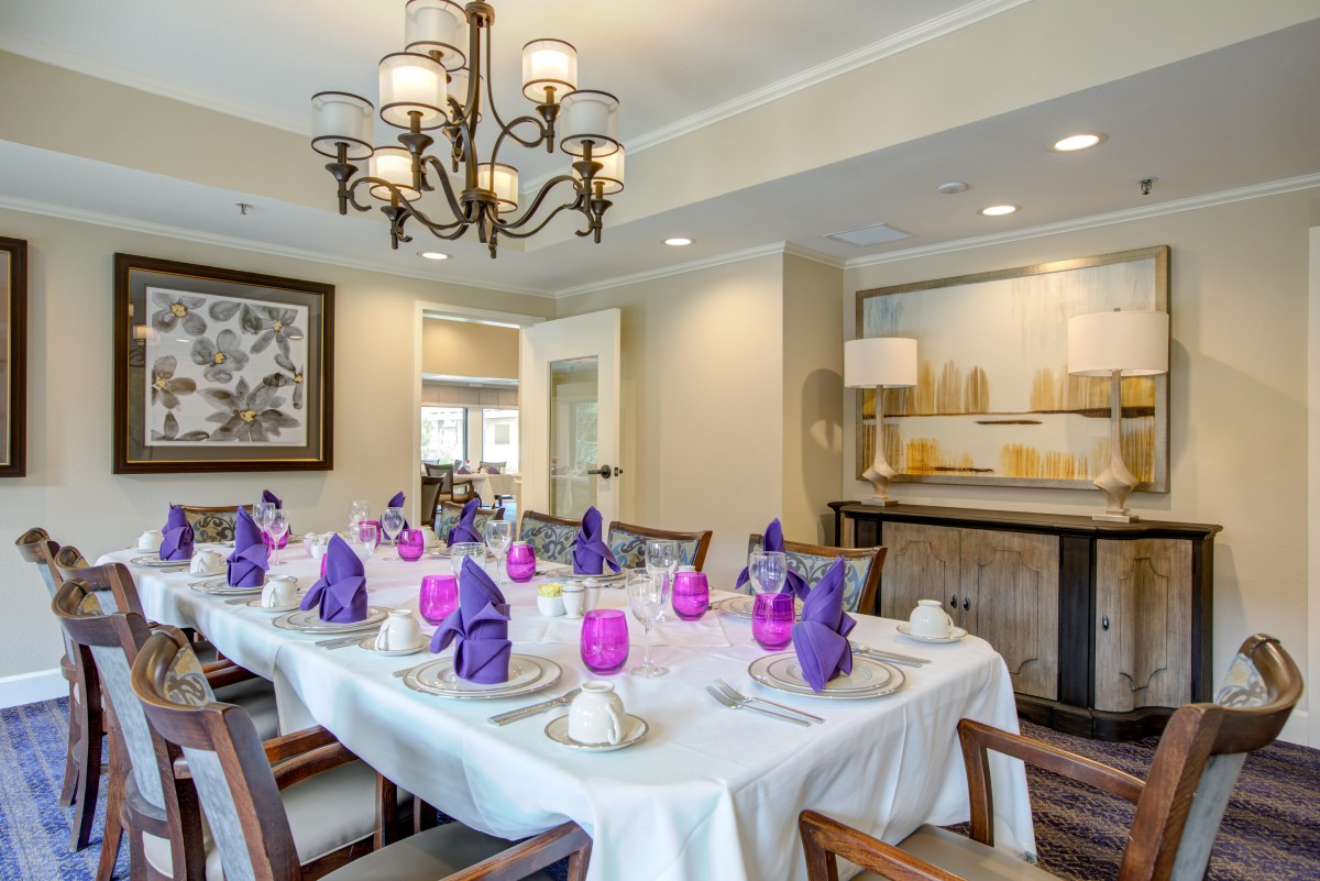 A well-decorated dining room with a table set for guests, featuring elegant purple napkins and a stylish chandelier.