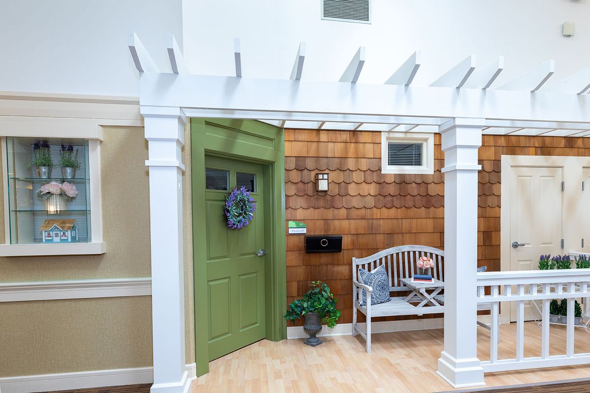 A cozy interior porch scene with a green door, decorative wreath, and white bench.