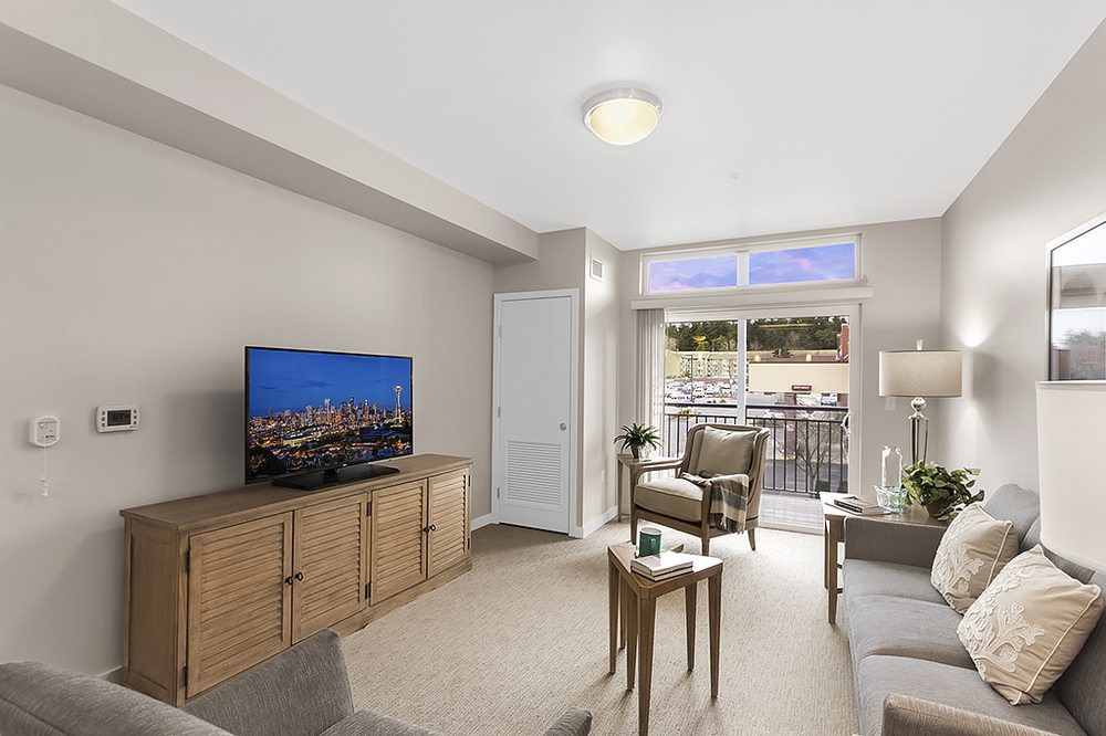 A modern living room with neutral tones, featuring a television, comfortable seating, and access to a balcony.